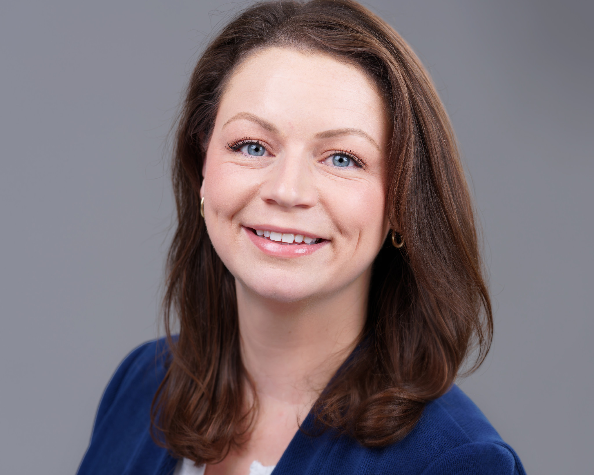 Studio headshot of a smiling woman in a blue cardigan against a gray background