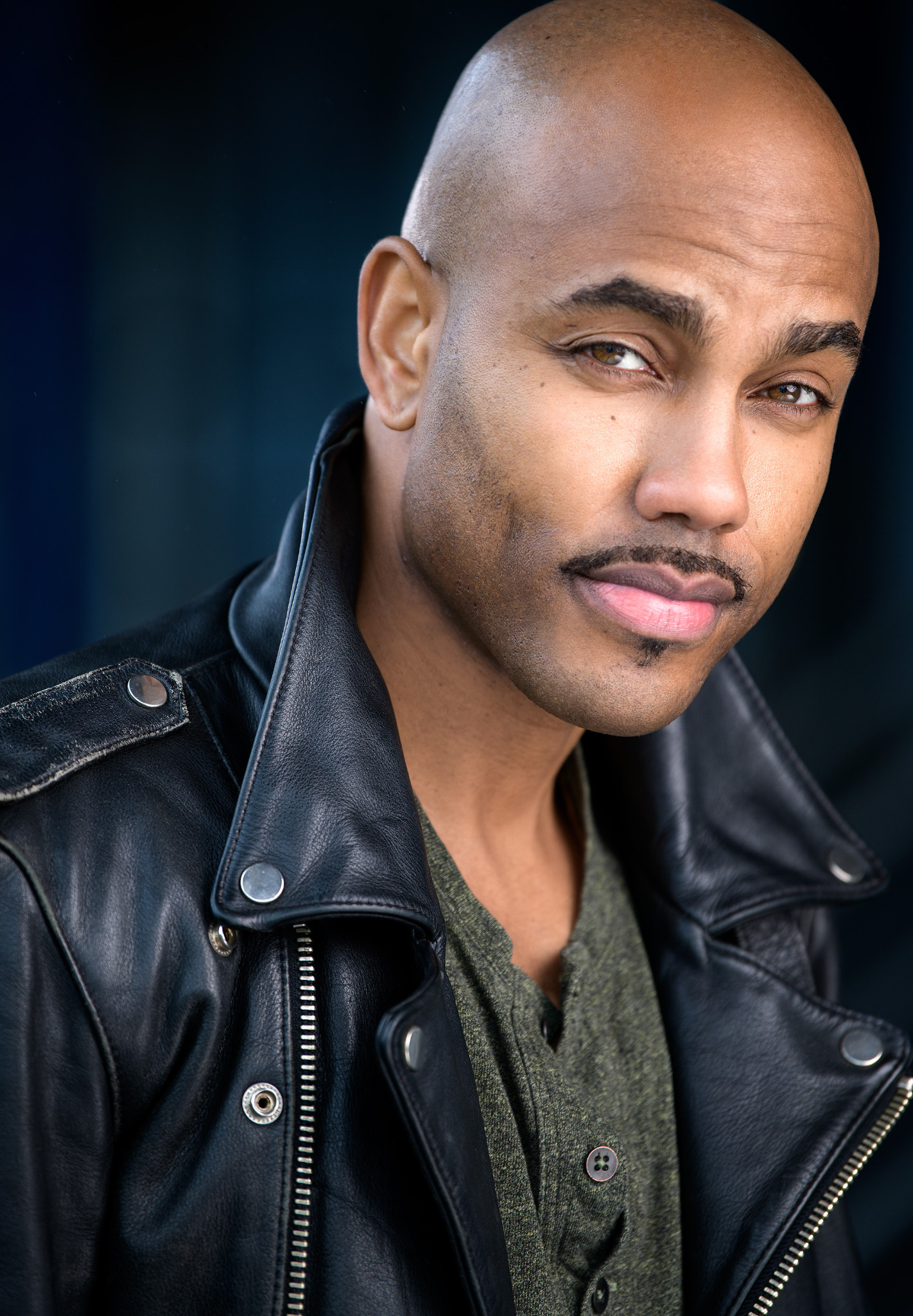 Vertical headshot of a man in a black leather jacket against a dark blue background