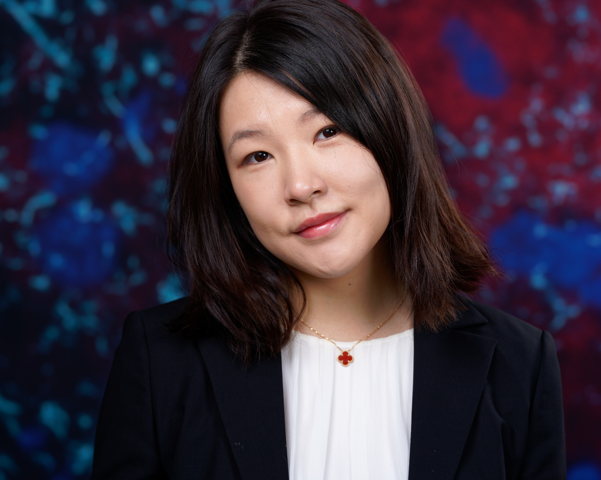 Headshot of a woman in a black blazer against a colorful blue and burgundy background