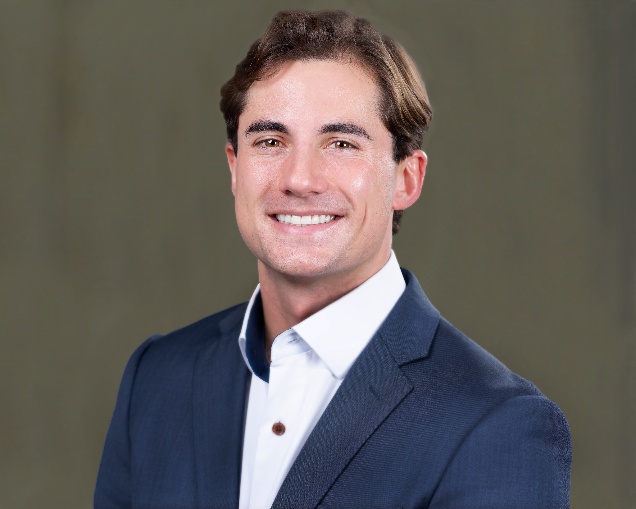 Smiling man in a navy jacket against an olive-gray studio background